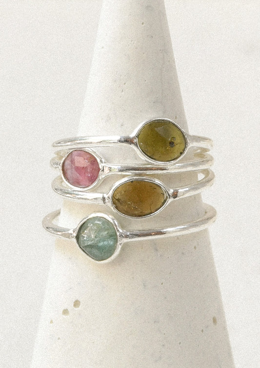 Four sterling silver rings stacked on top of one another with natural tourmaline stones in varying colors.