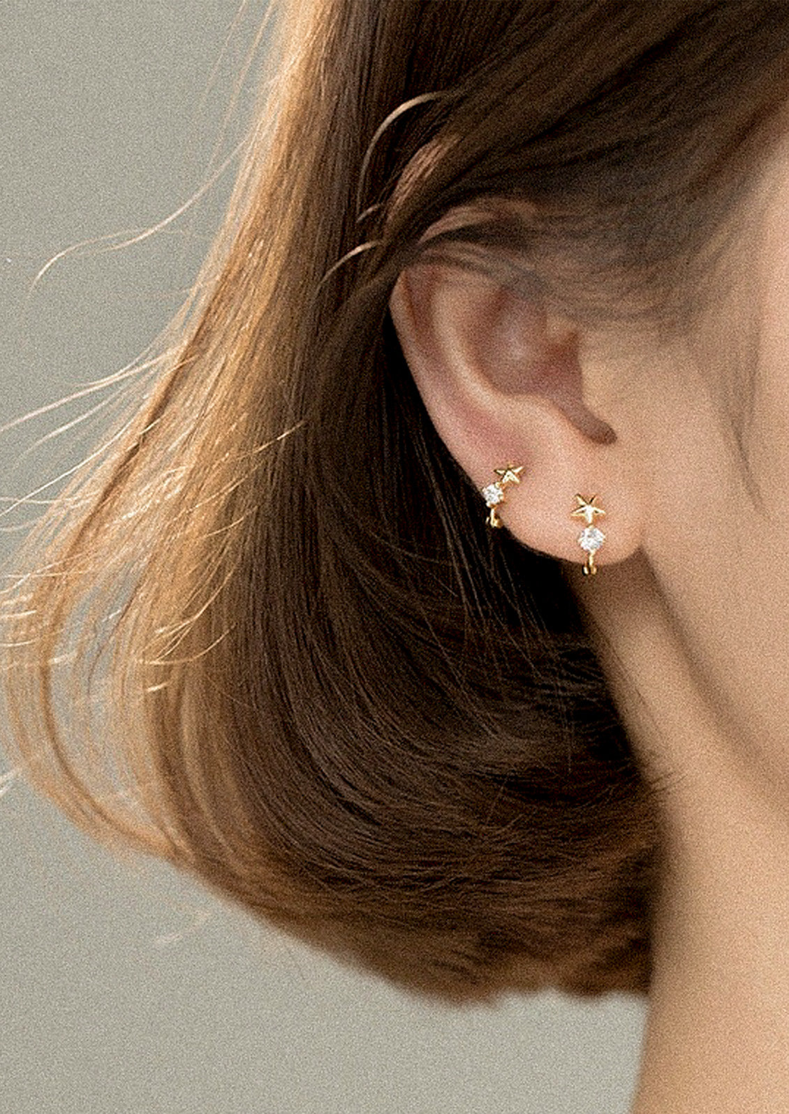 A woman wearing a pair of gold huggie earrings with a star design and a cubic zirconia gem.