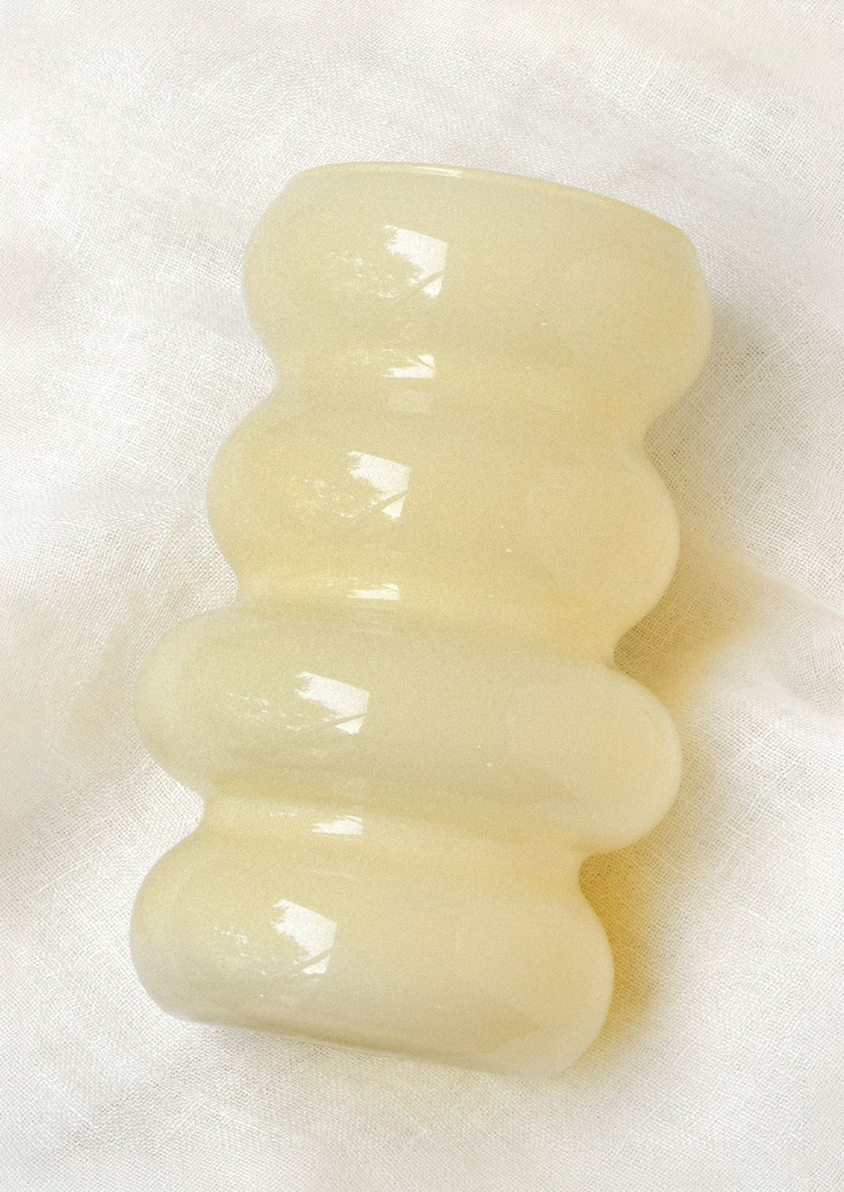A wavy glass vase in a butter yellow color.