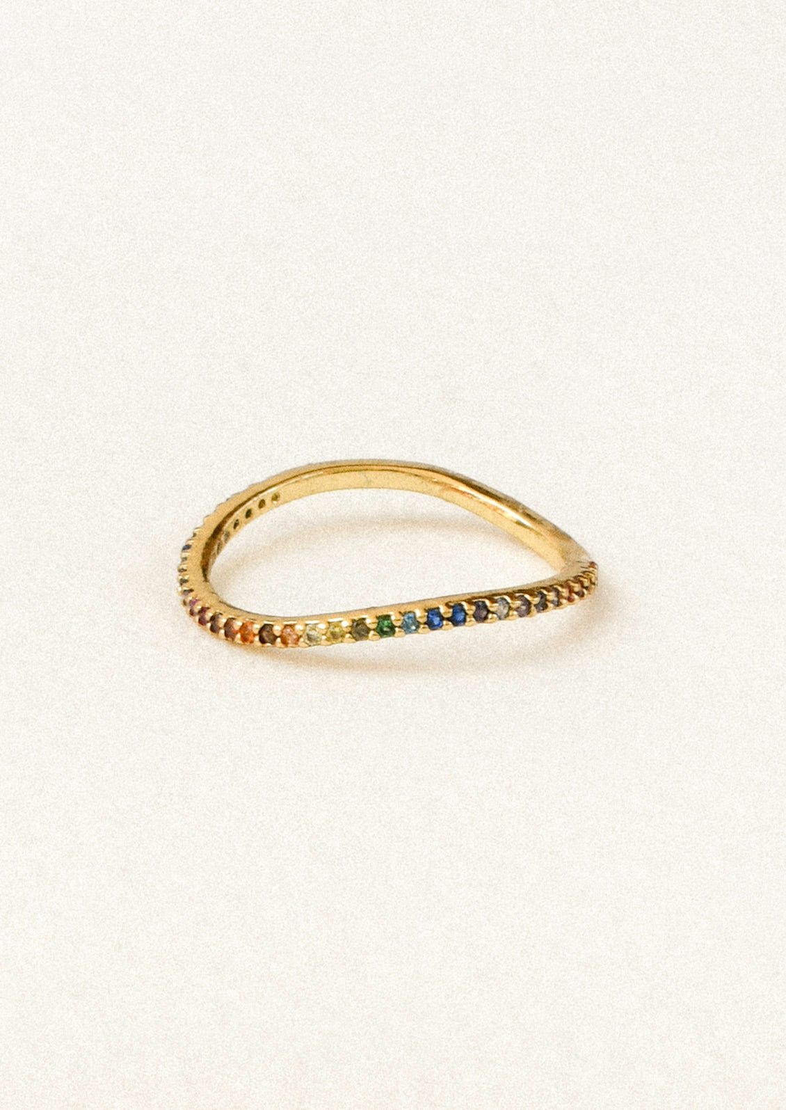 A gold ring with a bent wave design adorned with rainbow colored gems along the band.
