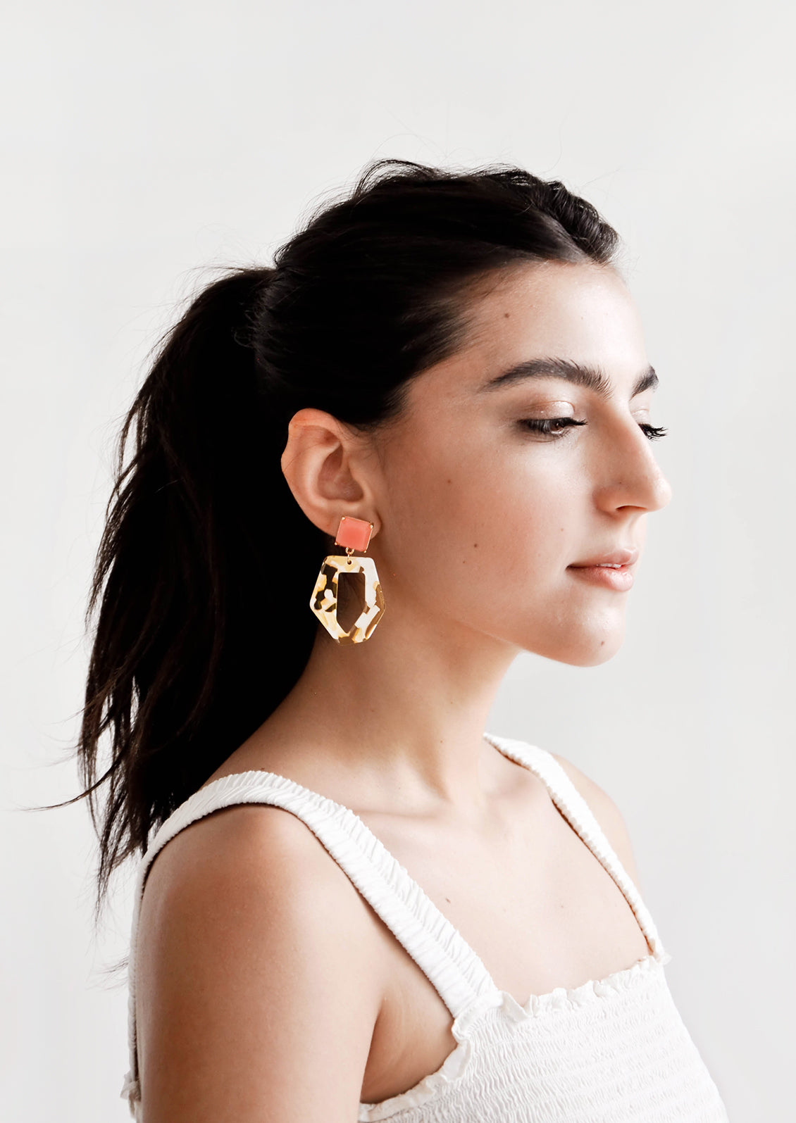 Model wears yellow, white, and coral pink drop earrings and white tank top.