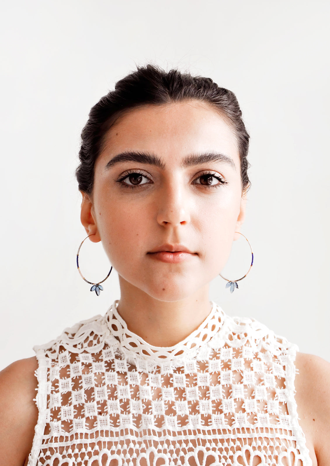 Model wears delicate beaded hoop earrings and white blouse.