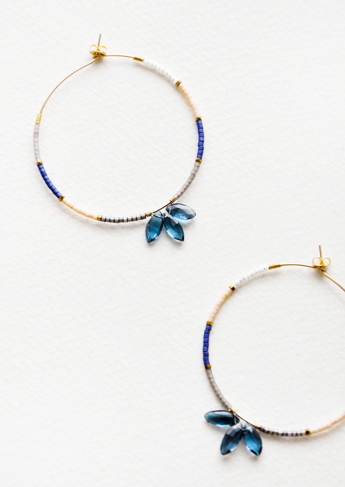 Delicate hoop earrings of blue and pink glass beads featuring a trio of larger blue beads at bottom center. 