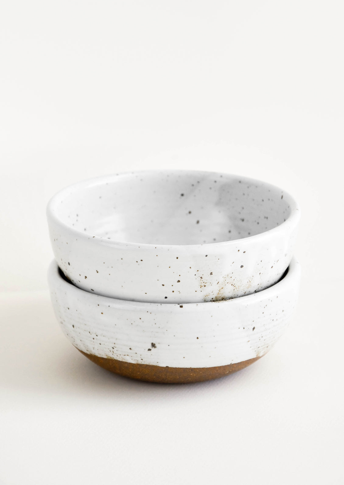 Two stacked white ceramic bowls with brown speckles.