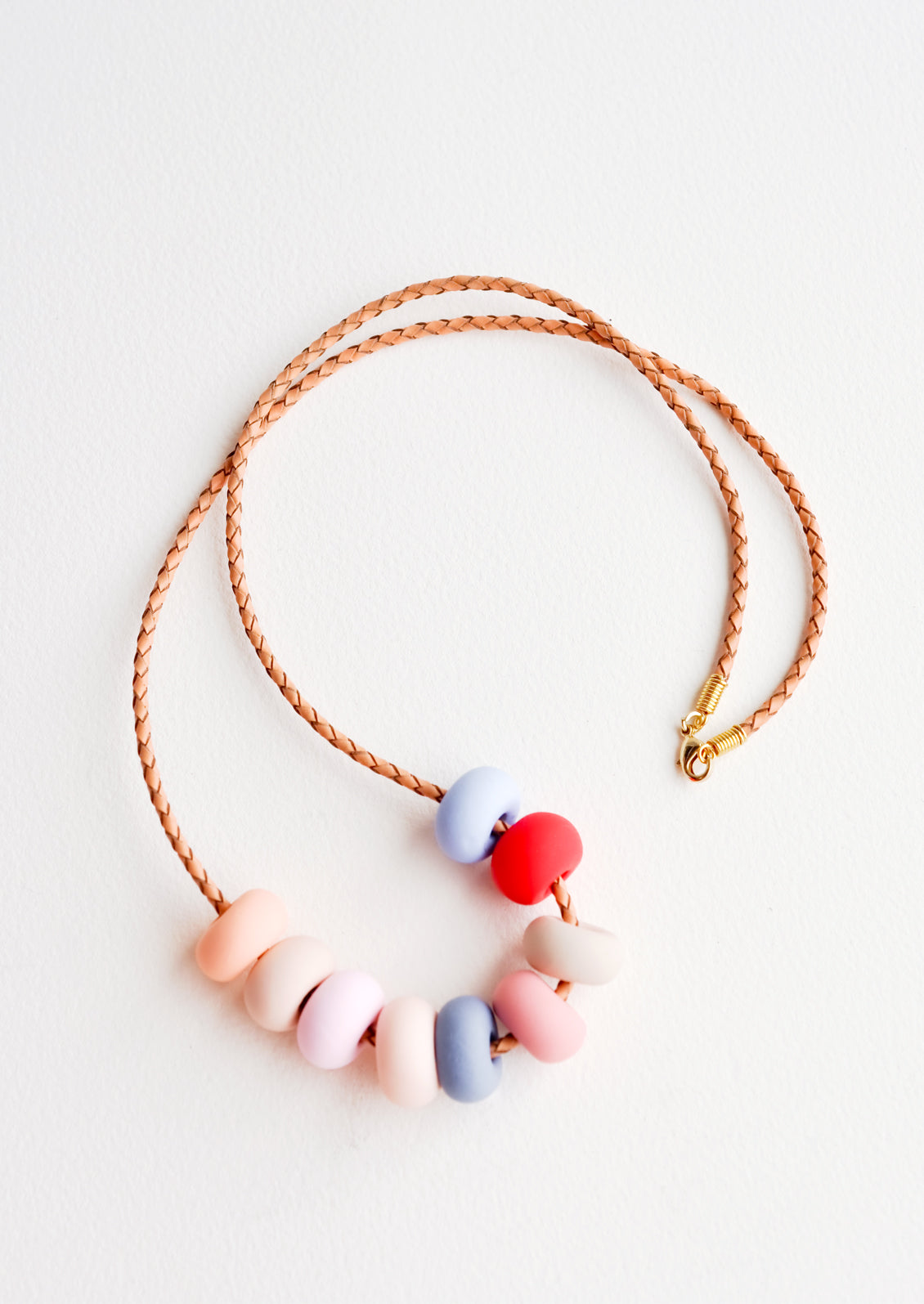 Woven leather cord necklace with gold clasp and rounded clay beads tans, pinks, red, and blues.