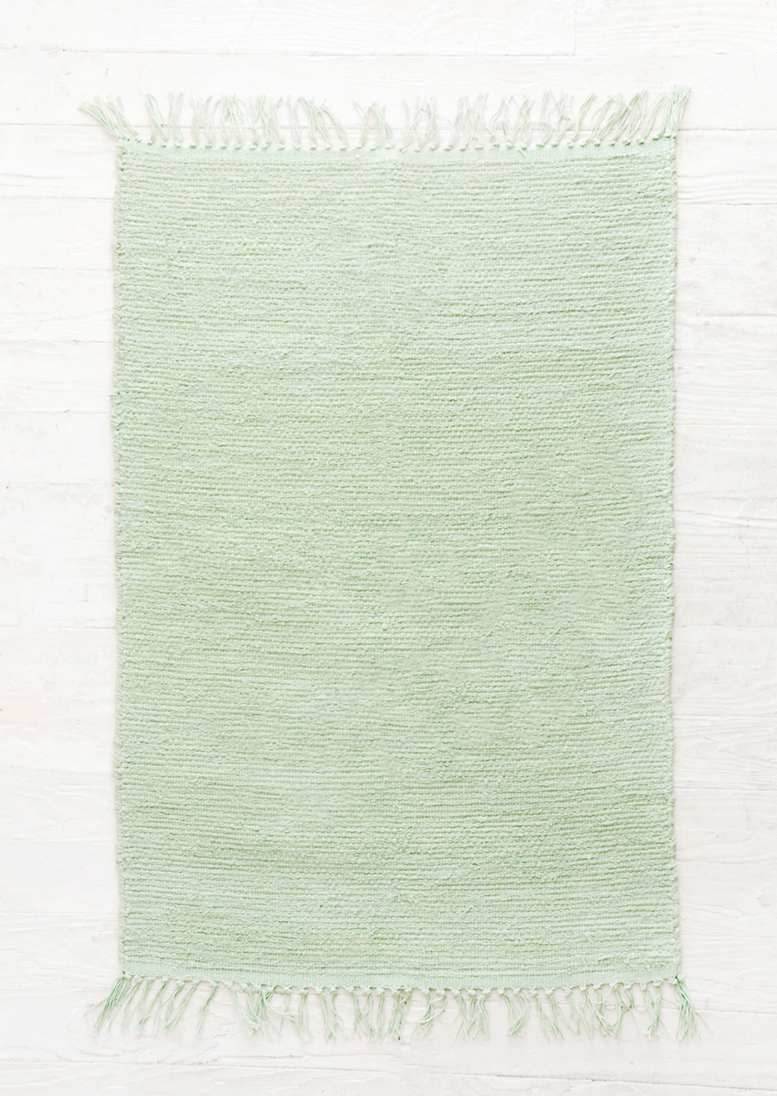 Cotton flatweave rug in solid mint green color with slight texture, fringe trim on two ends