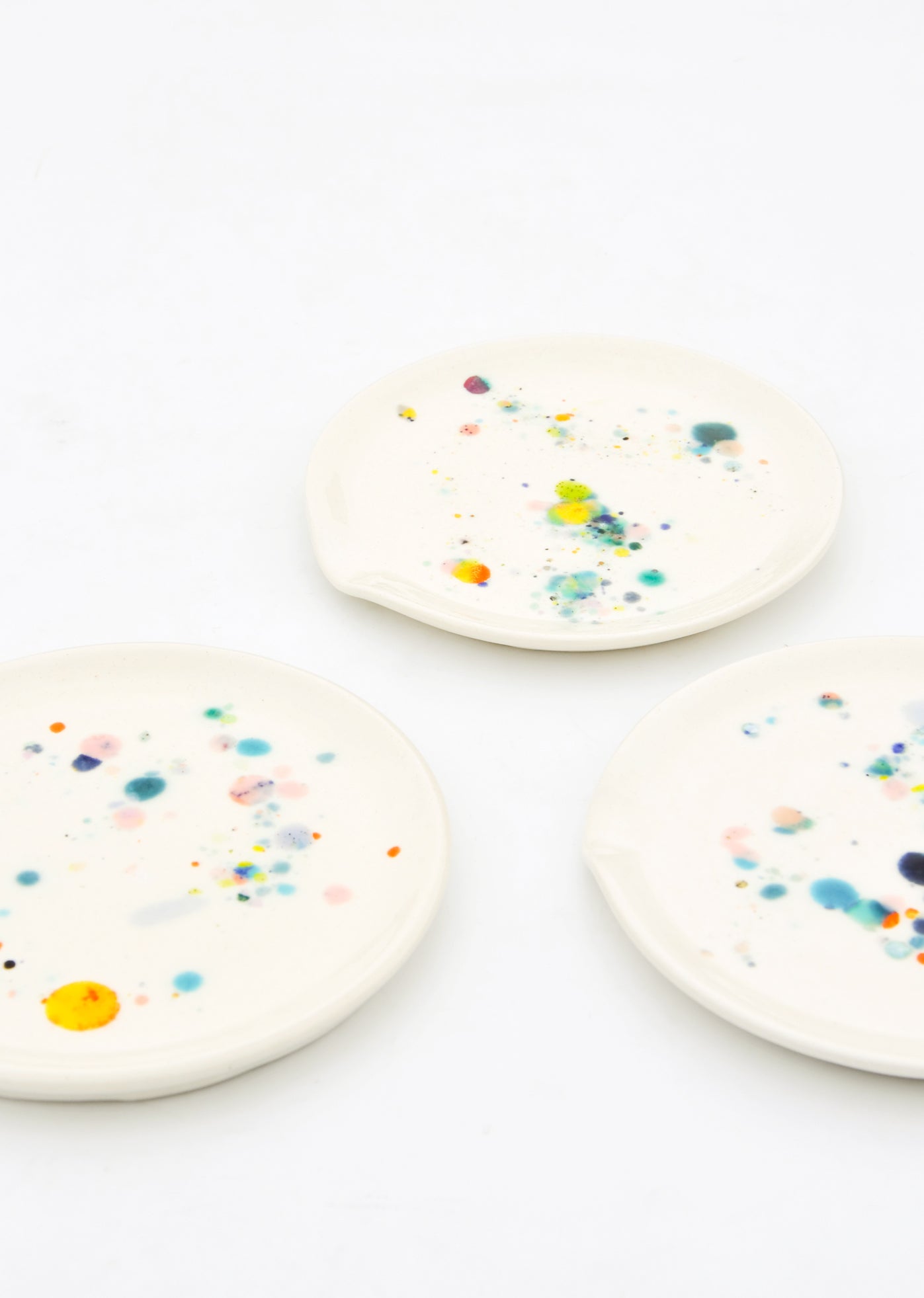 Three ceramic spoon rests in ivory with splattered colorful glaze drips.