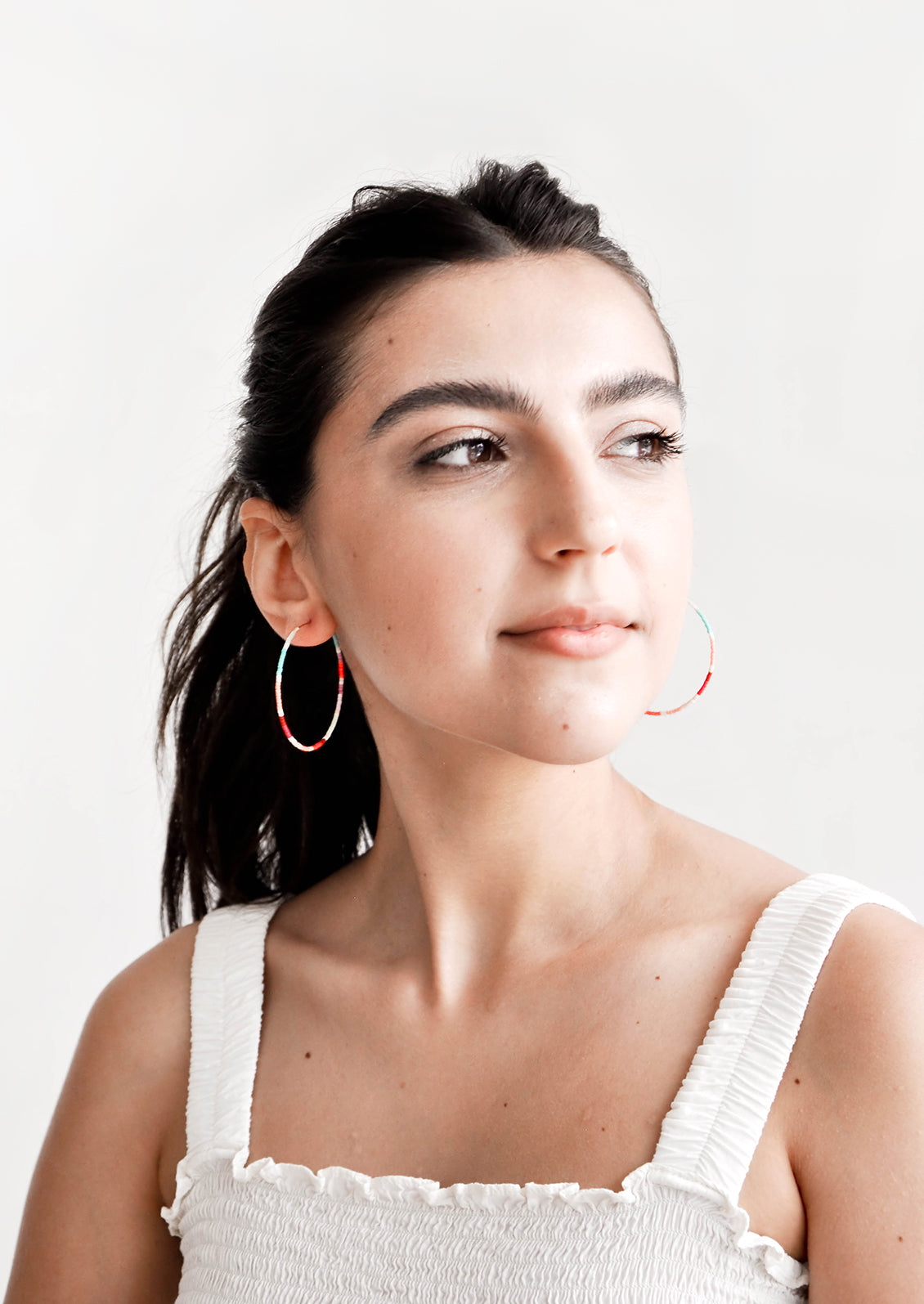 Model wears multi-colored hoop earrings and white tank top.