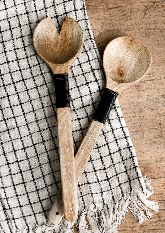 A pair of wooden salad servers with decorative black wire wrapping on handle.