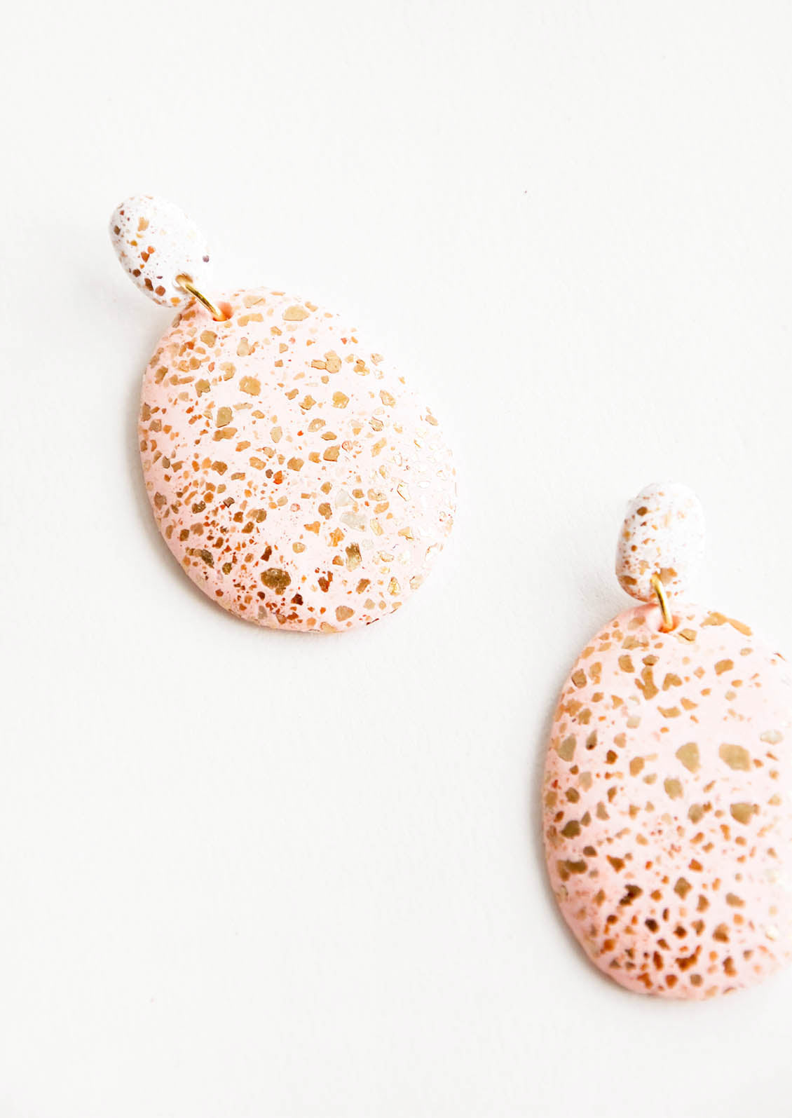 Dangling glitter covered earrings, with a blush pink larger oval dangling from a small white bead.