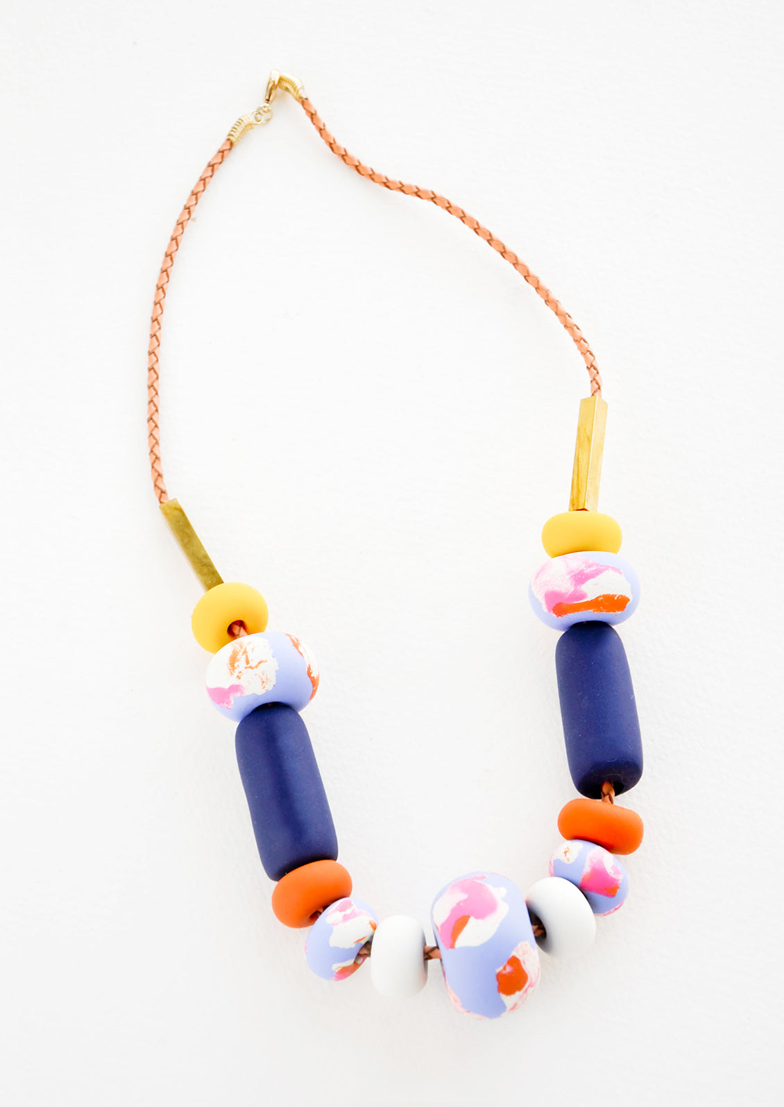 Necklace with gold clasp, brown woven leather cord, rectangular brass beads, and beads of varying shapes and sizes in yellows, pinks, blues, and oranges.