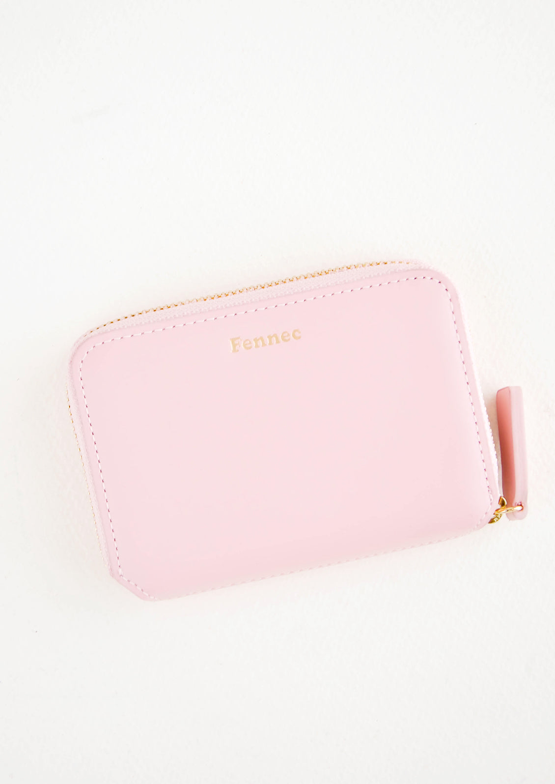 Pale pink leather zip wallet with brand name Fennec embossed in small gold letters at top center of wallet face.