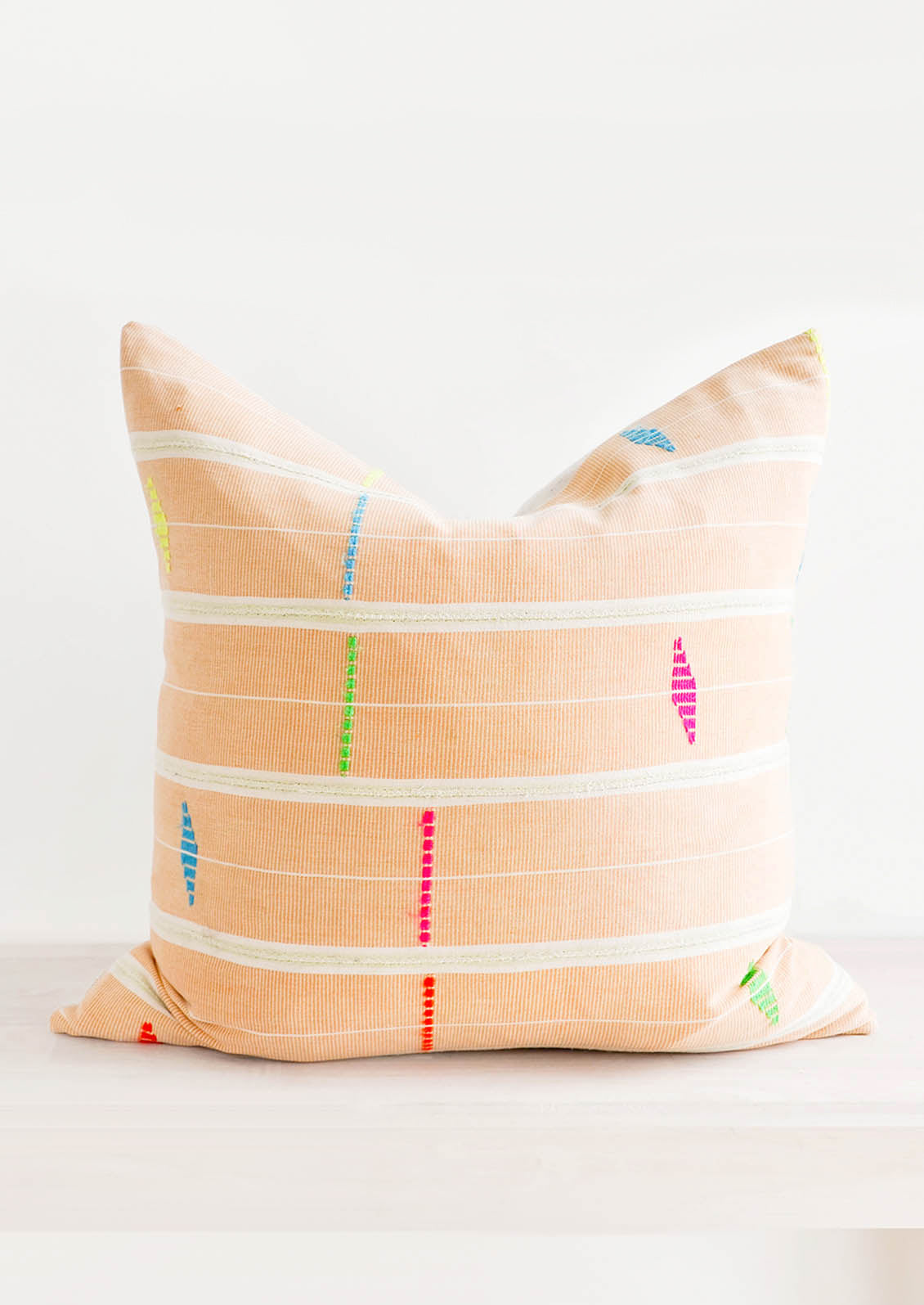 Square throw pillow made from vintage African fabric in bright orange with neon embroidery details.