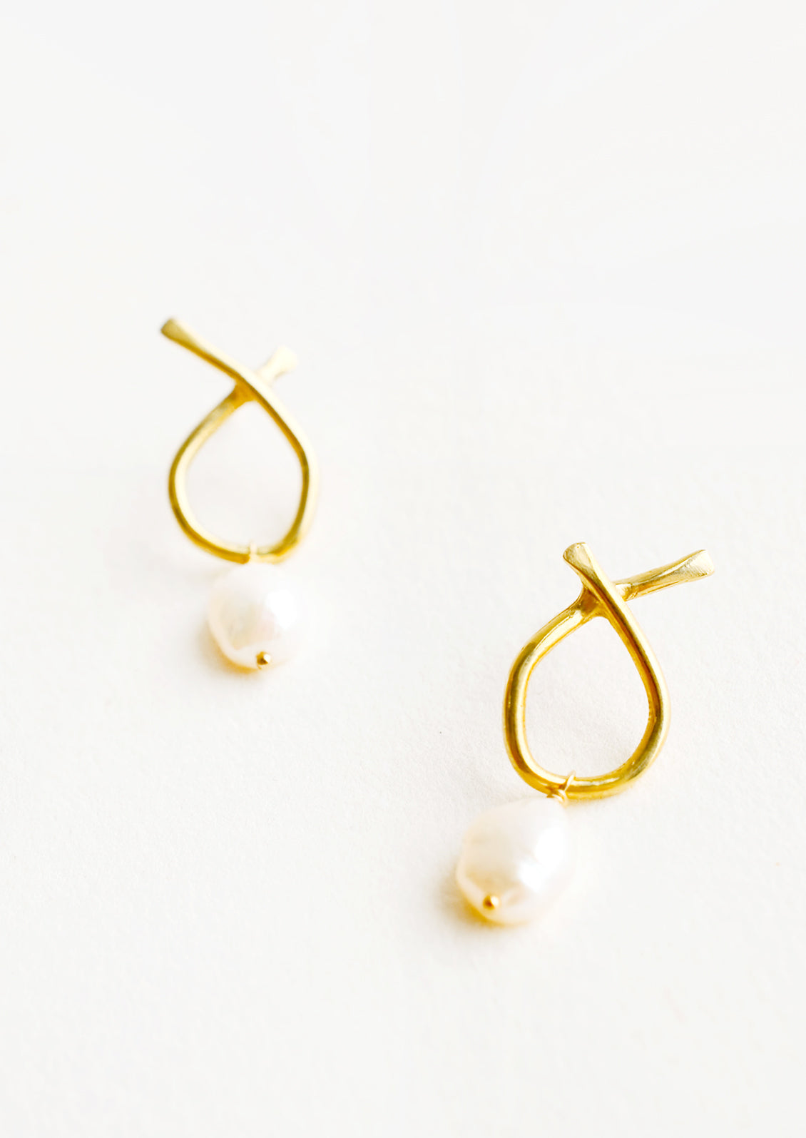 Pair of brass earrings featuring a slim asymmetrical frame on a post back and dangling pearl.