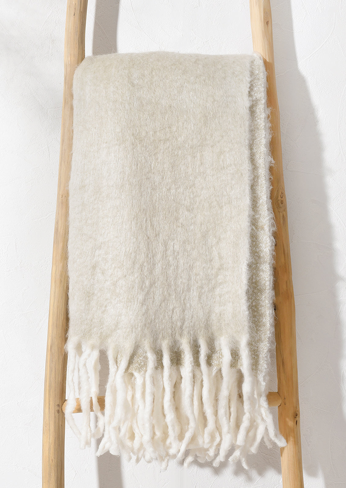A beige mohair blanket hanging on a ladder.