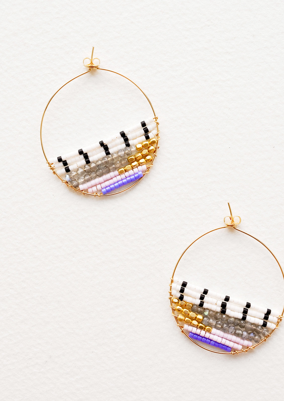 Thin gold hoop earrings with beads in white, black, gold, gray, and purple filling bottom half of hoop.