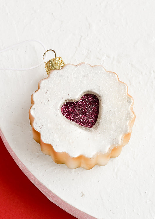 A glass holiday ornament in shape of raspberry linzer cookie with heart center.