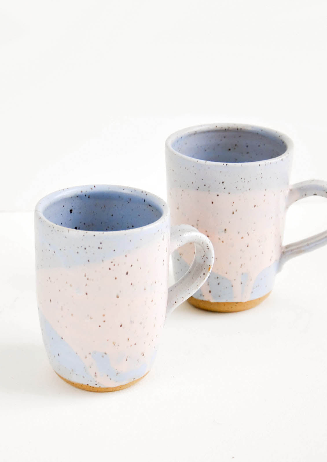 Two ceramic mugs in blue and pink with brown speckles.