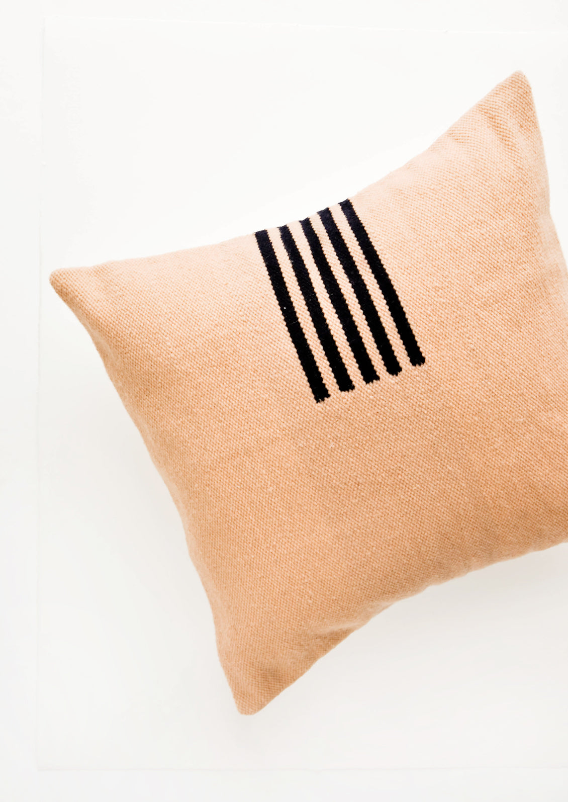 Peach colored, square wool throw pillow with contrasting small stripe detail at side.