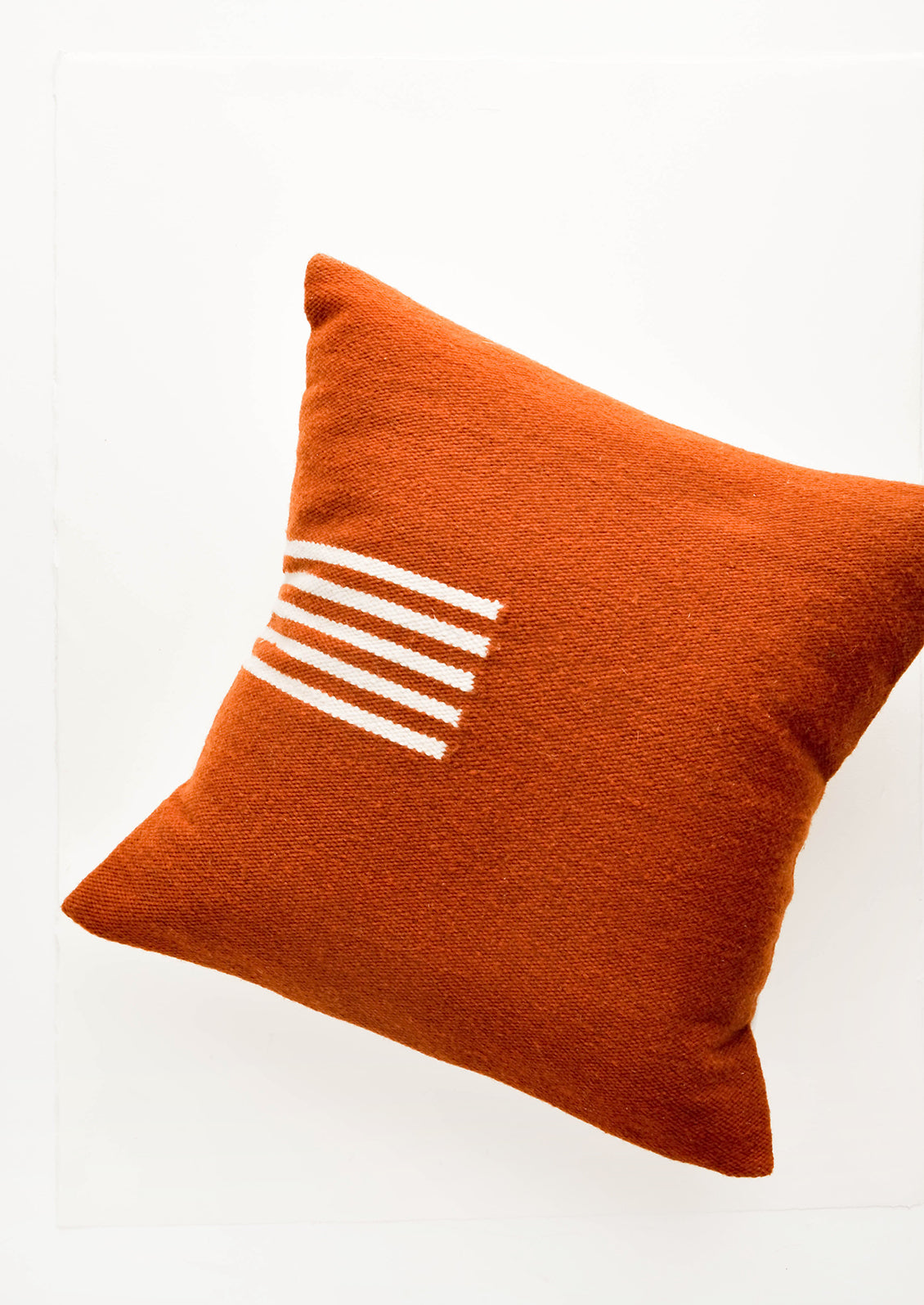 Terracotta colored, square wool throw pillow with contrasting small stripe detail at side.