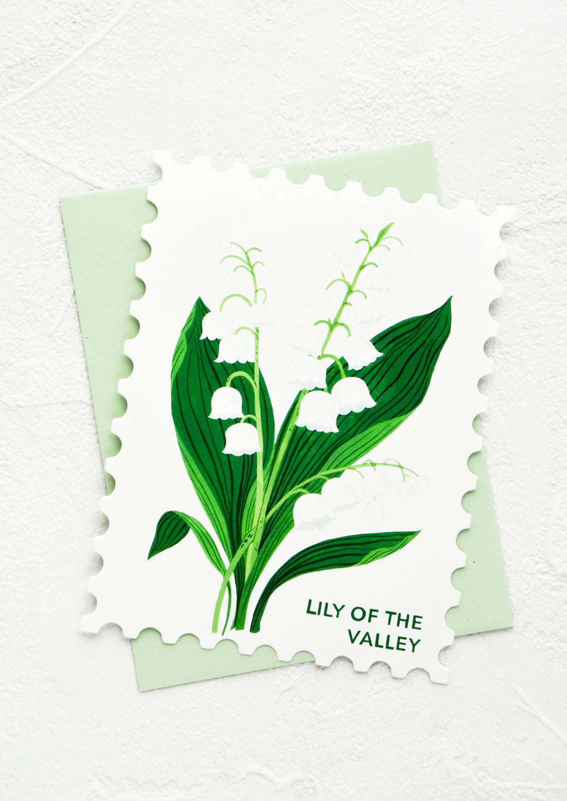 Diecut greeting card in the shape of a postage stamp, printed graphic of Lily of the Valley floral.