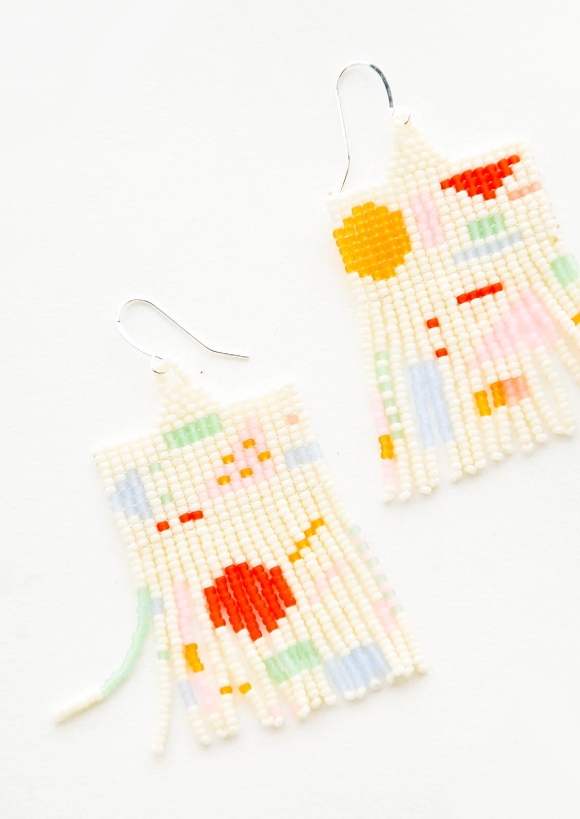 Cream colored glass bead fringe earrings with pattern of colorful geometric shapes on silver ear wire.