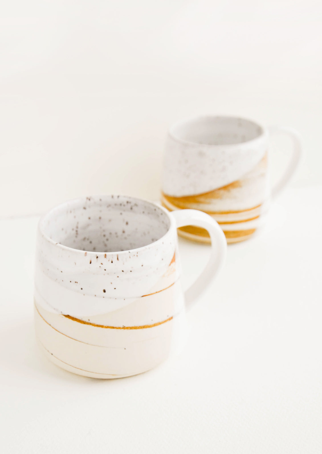Two ceramic mugs with handles in swirled ivory and brown clay with speckled white glazed rim.