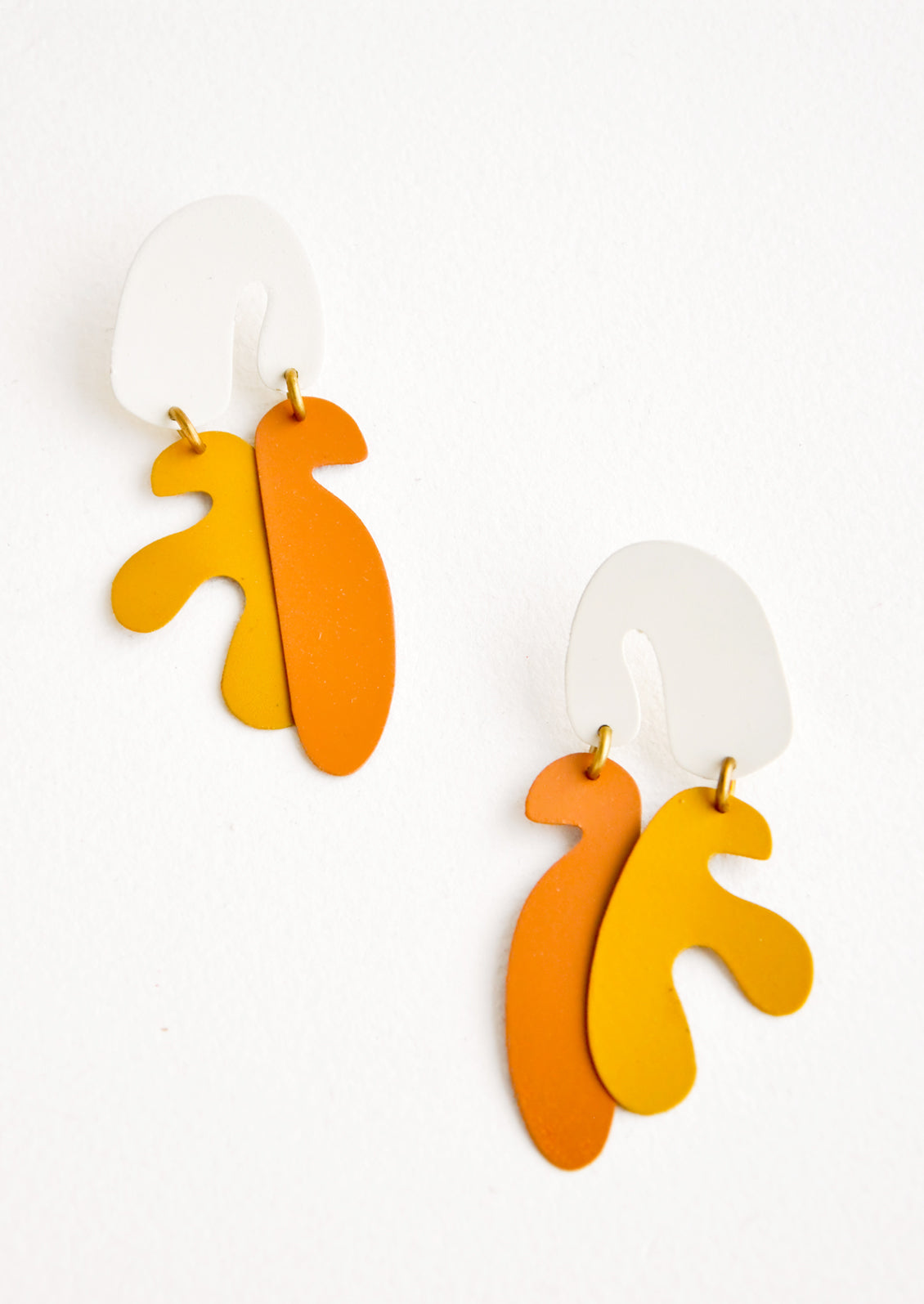 Dangling post earrings with orange and yellow organic seaweed shapes hanging from a white arced shape, connected by small brass rings.
