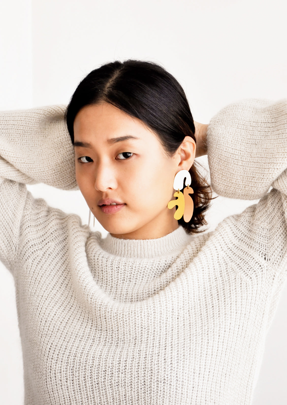 Model shot of woman wearing earrings and white sweater.