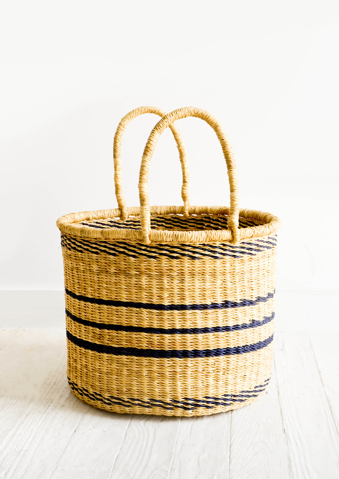 Round straw storage basket with handles at top and navy blue stripes throughout
