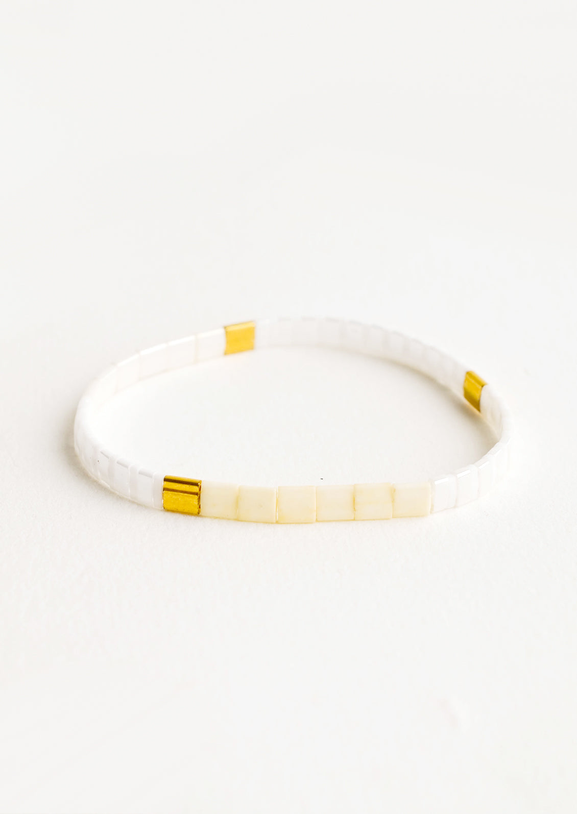 Bracelet featuring flat white beads interspersed with flat gold bead on an elastic cord.