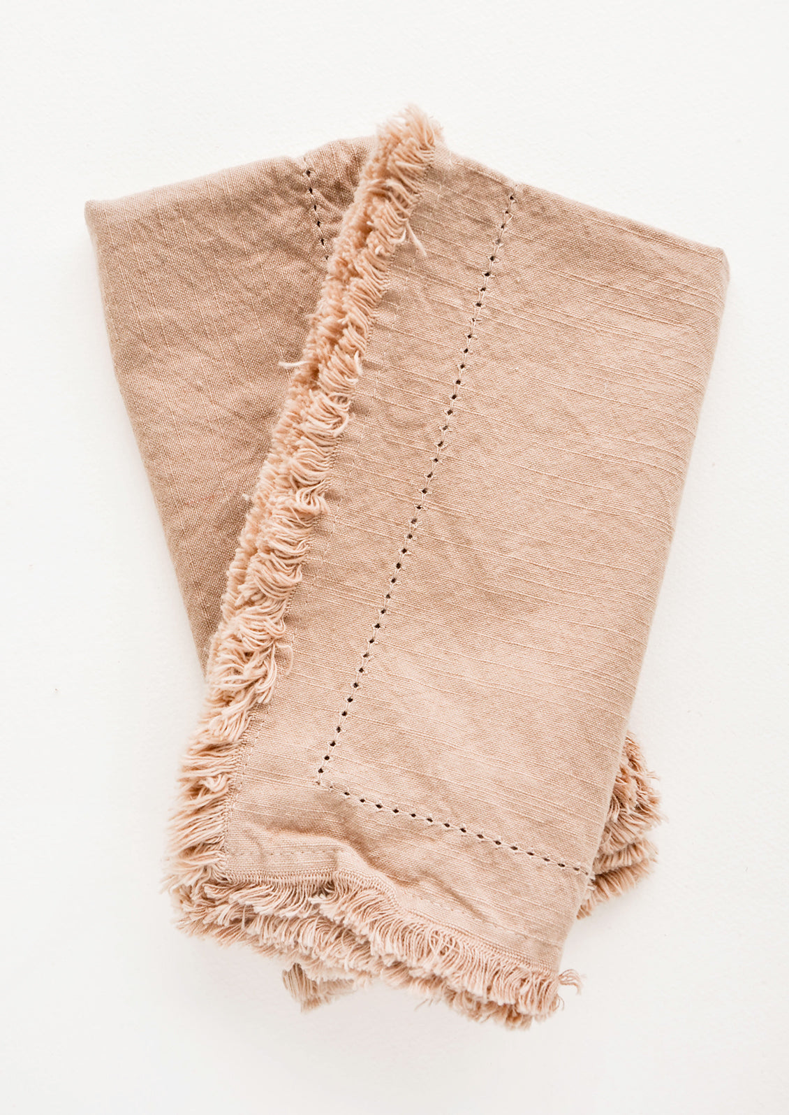 Two folded tan Cotton Napkins with frayed edges .